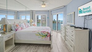 A bedroom with a bed, a nightstand, a dresser, a TV, and a balcony with a view.