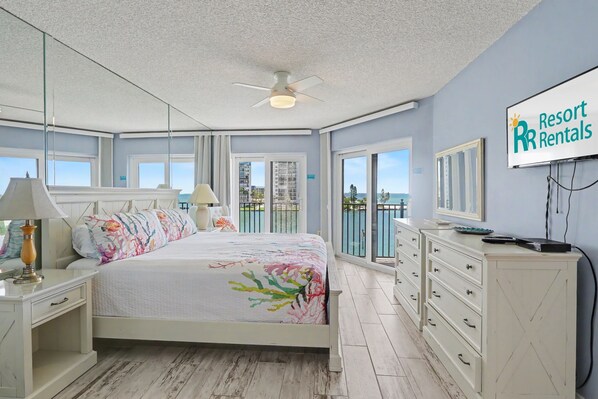 A bedroom with a bed, a nightstand, a dresser, a TV, and a balcony with a view.