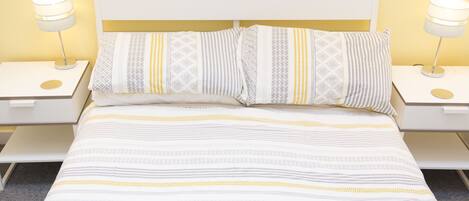 A neatly made bed with patterned bedding and two bedside tables with lamps.