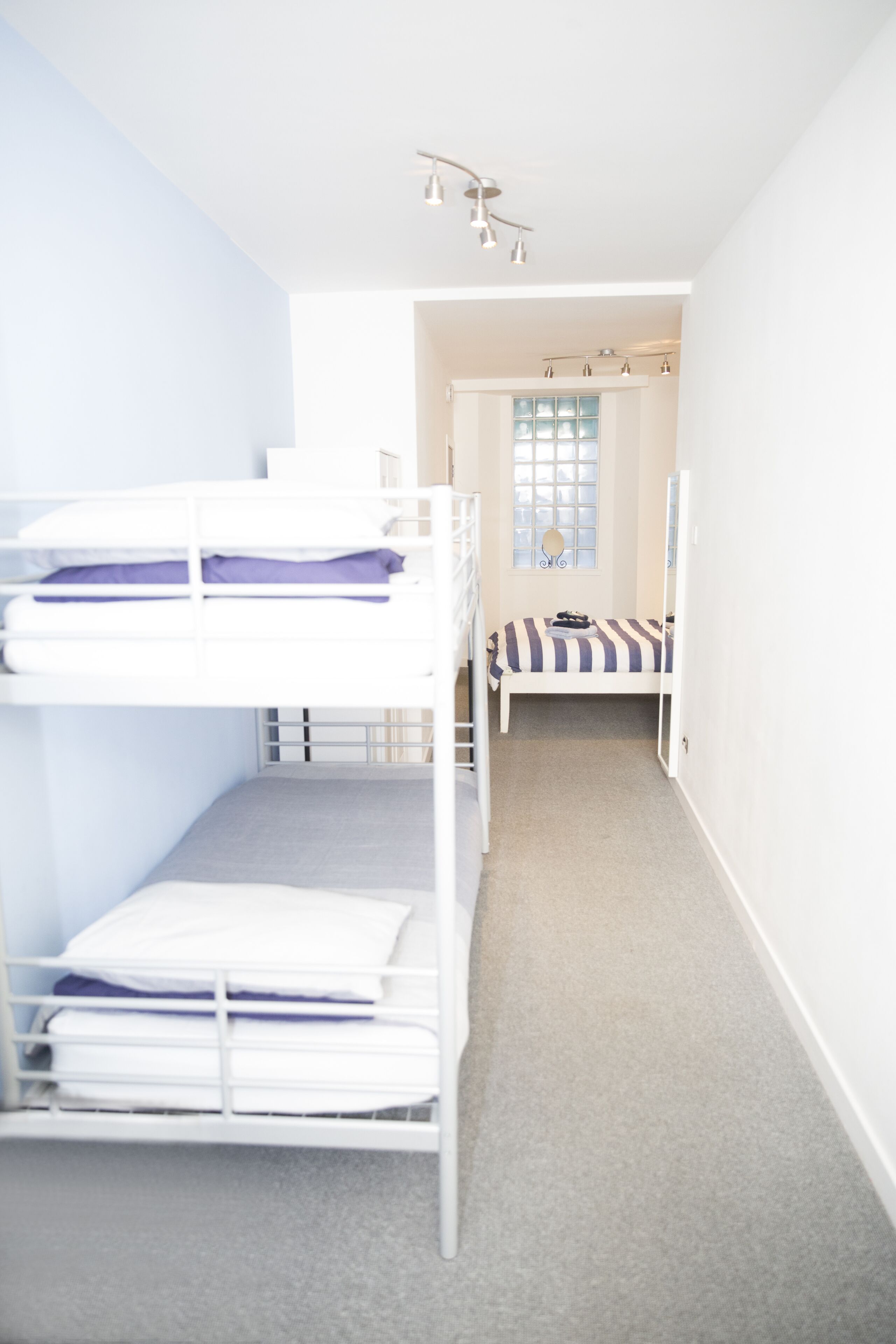 Een slaapkamer met een stapelbed, een raam en een deur die naar een andere kamer leidt.