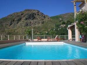Une piscine avec des chaises longues en bois et vue sur une montagne.