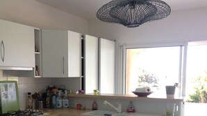 Una cocina moderna con gabinetes blancos, lavavajillas empotrado, estufa a gas y ventana con vista a la vegetación.