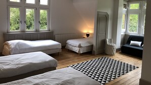 Una habitación con dos camas individuales, un sofá pequeño, un tapete estampado y una ventana con vistas a zonas verdes.