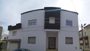 A modern two-story building with a flat roof, a front entrance with a small porch, and a car parked in front. - Maison des Tulipes (Béni Khiar)