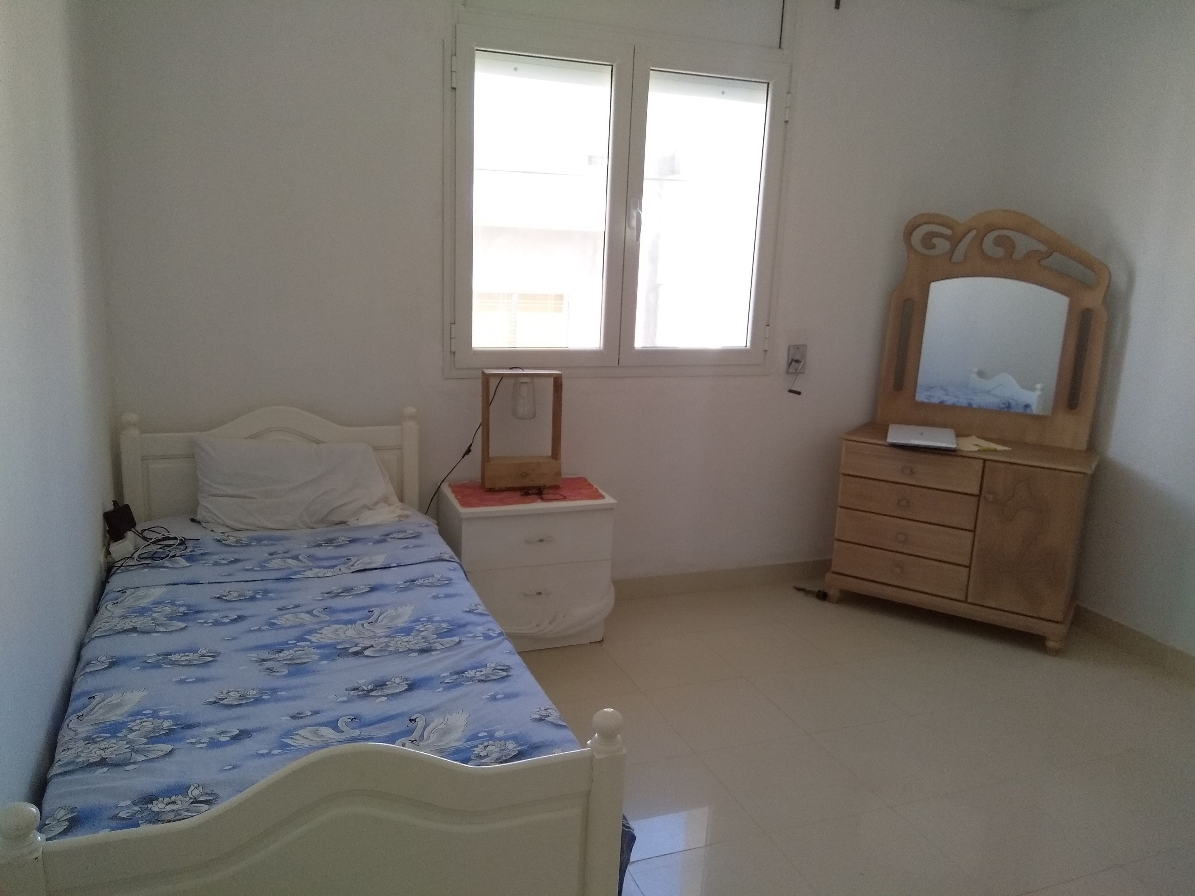 Une chambre à coucher avec un lit, une table de chevet, une commode et une fenêtre.