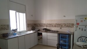 A kitchen with white cabinets, a gas stove, a sink, and a refrigerator. - Maison des Tulipes (Béni Khiar)