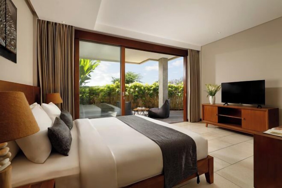 A hotel room with a bed, a TV, a sliding glass door to a balcony, and a small table.