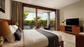 Quarto de hotel moderno com uma cama grande, televisão de tela plana, uma mesa pequena e vista para um jardim exuberante através da porta de vidro deslizante.