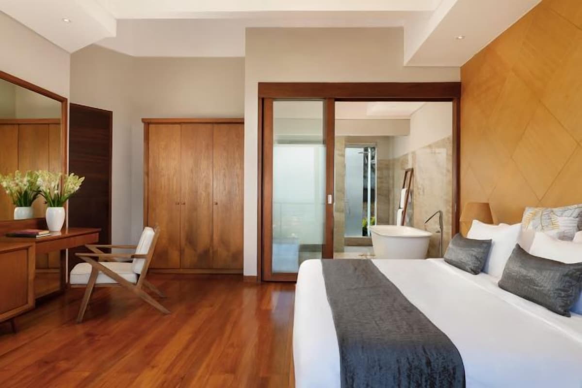 Ein modernes Hotelzimmer mit einem großen Bett, Holzmöbeln, einem Schreibtisch und einem Badezimmer mit einer Badewanne.