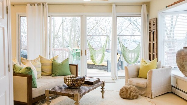 Un salón luminoso con un sofá, sillones, una mesa de centro y un ventanal con cortinas.