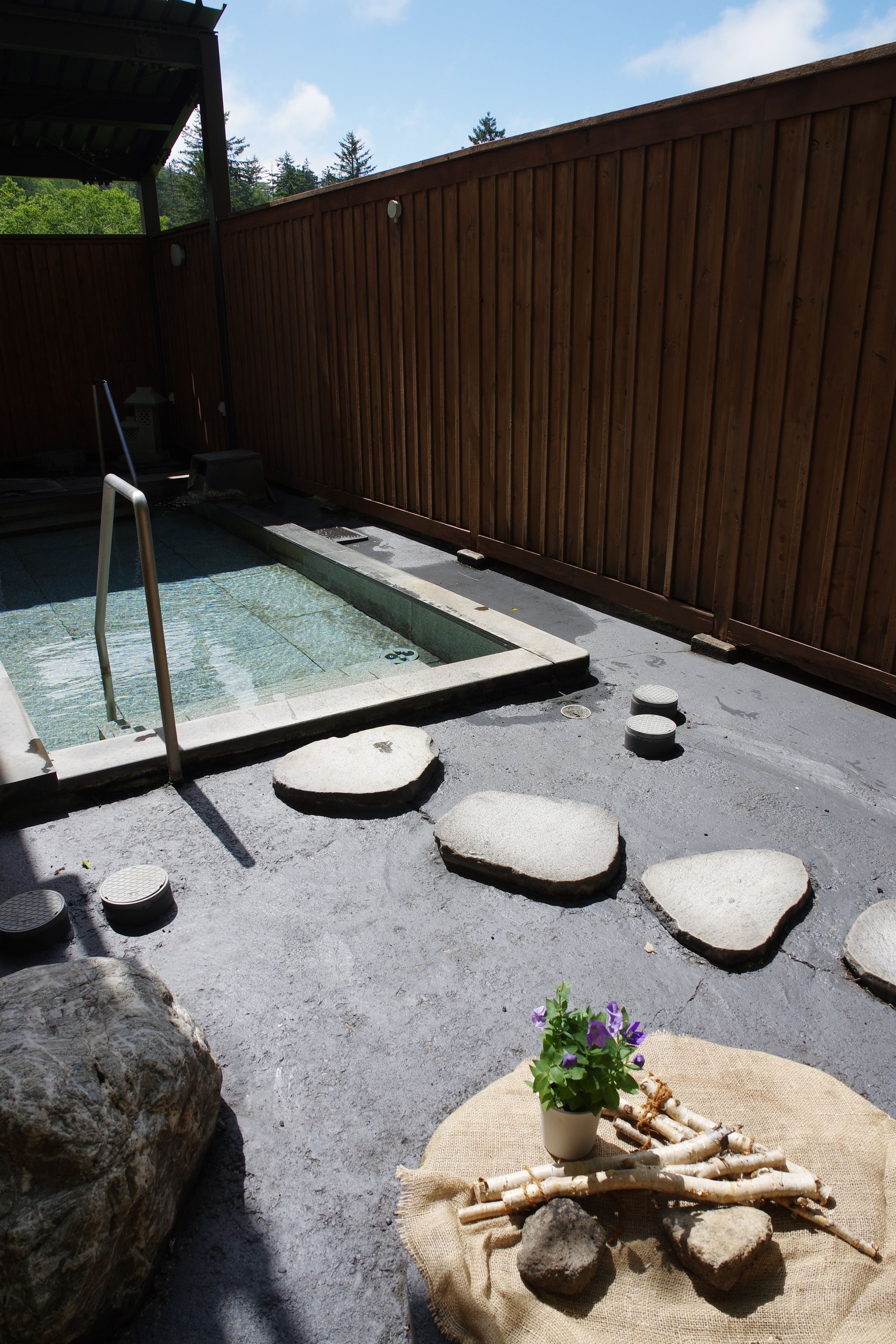 A backyard with a hot tub, a wooden fence, and a small garden area with rocks and a potted plant.