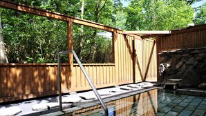 A wooden deck with a stone pathway leading to a pool area, surrounded by lush greenery. - K's House Hokkaido - Asahidake Onsen Hostel (Higashikawa)