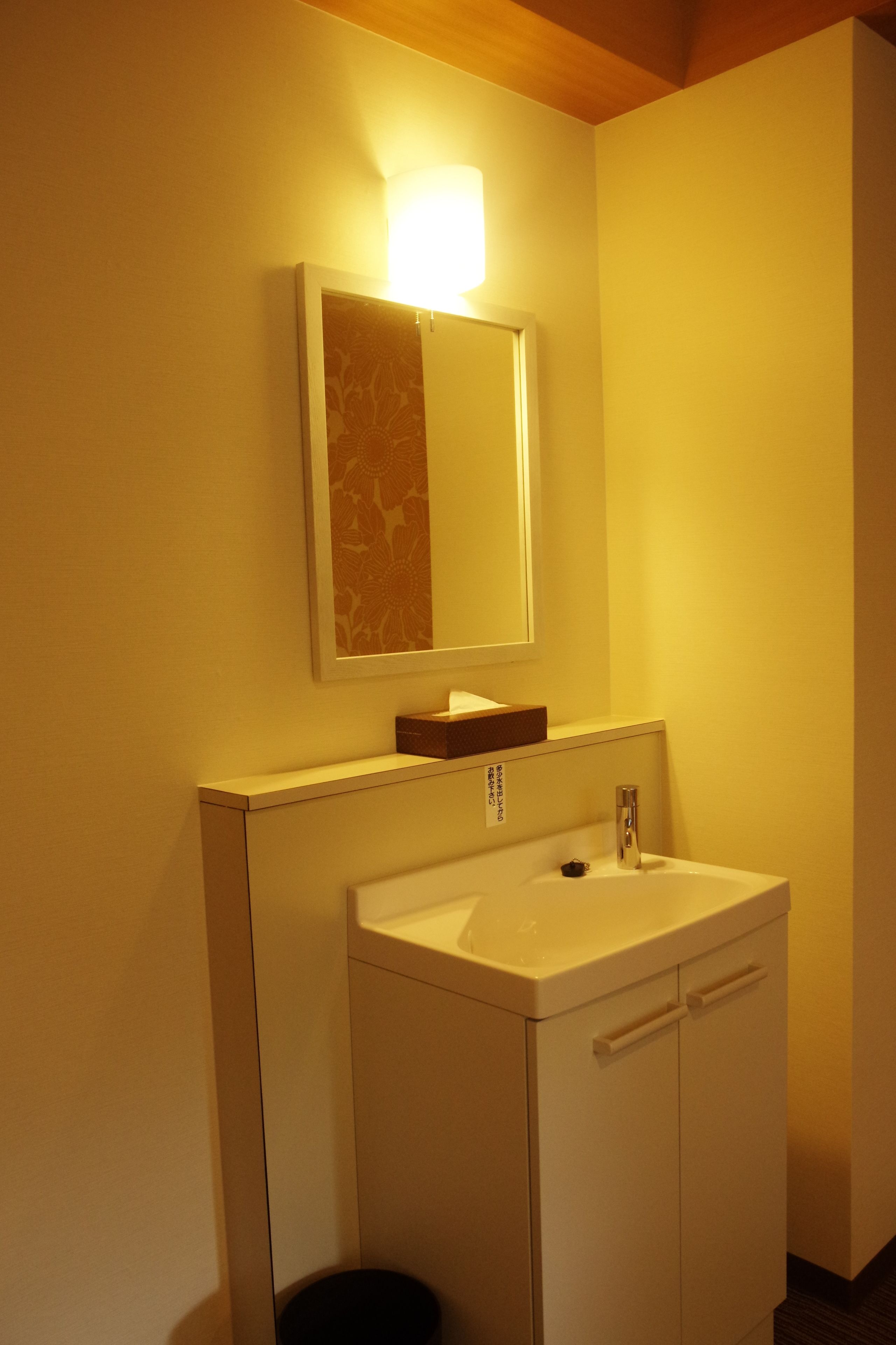 A bathroom with a white sink, a mirror, and a light fixture above the mirror.