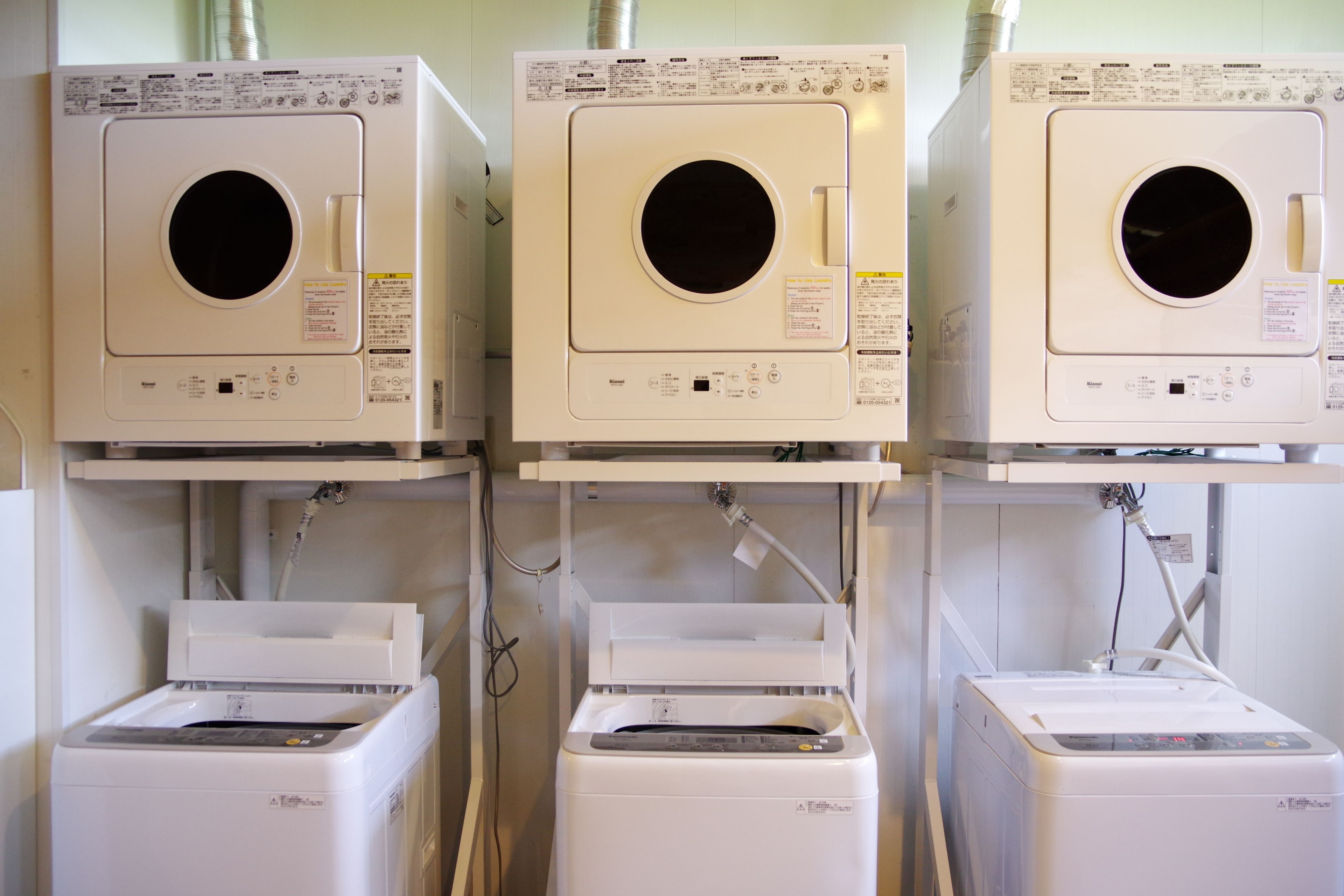 Three stacked washing machines with control panels and hoses.