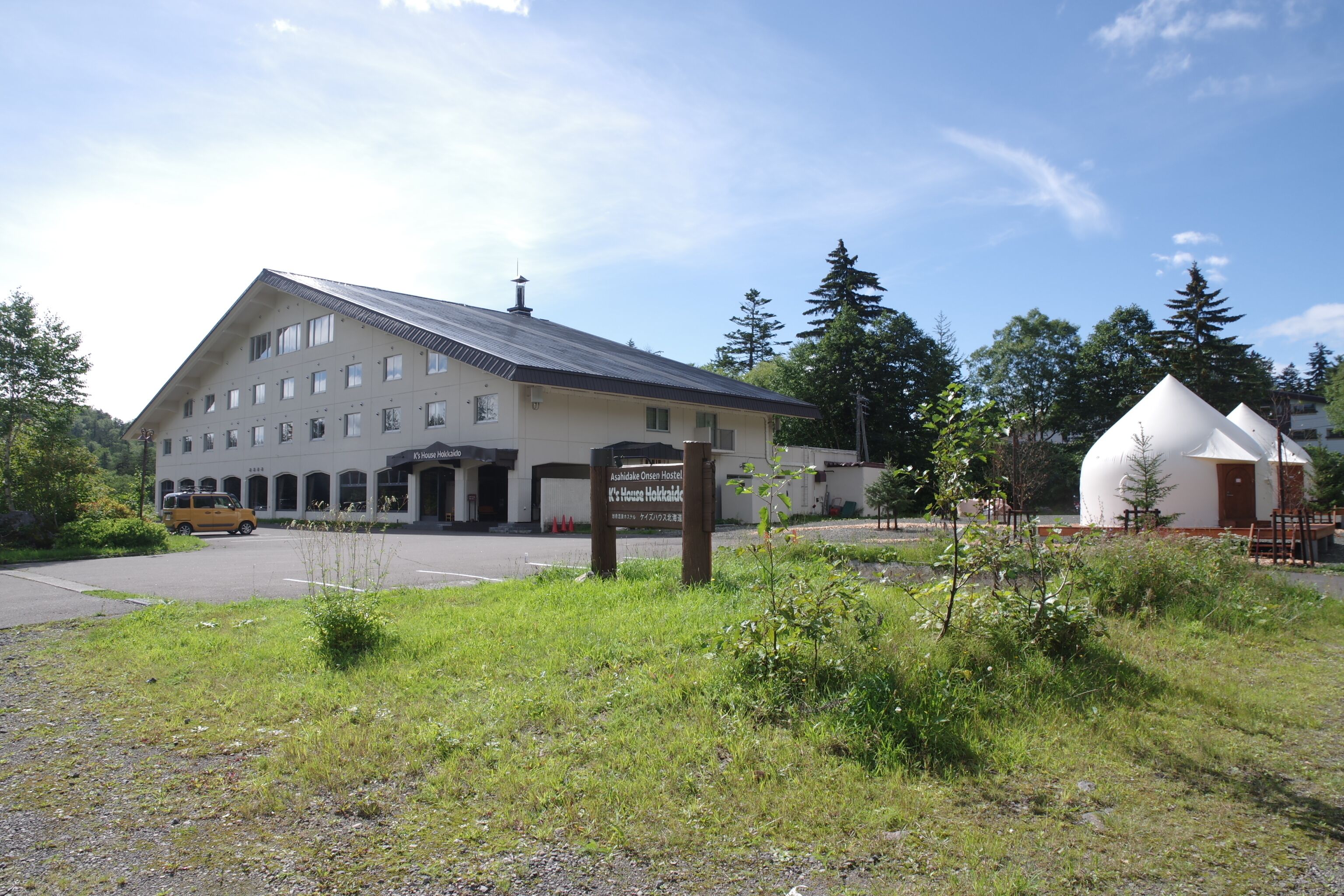 A large building with a sign for the K's House Hotel, a parking area, and a small white structure nearby.