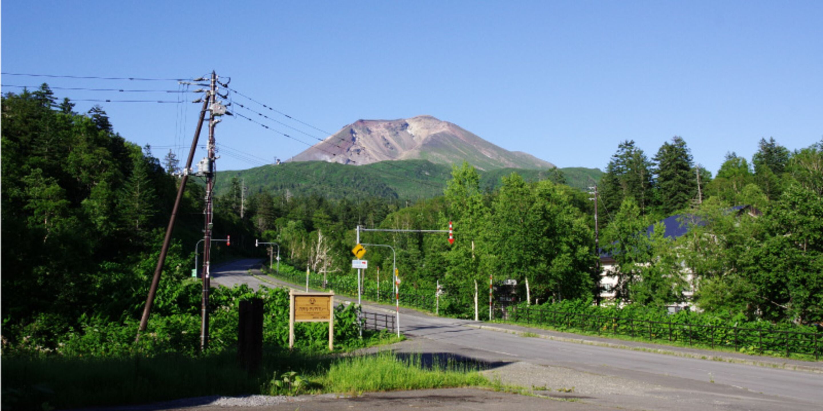 A road leading to a mountain with a traffic light and a signboard.