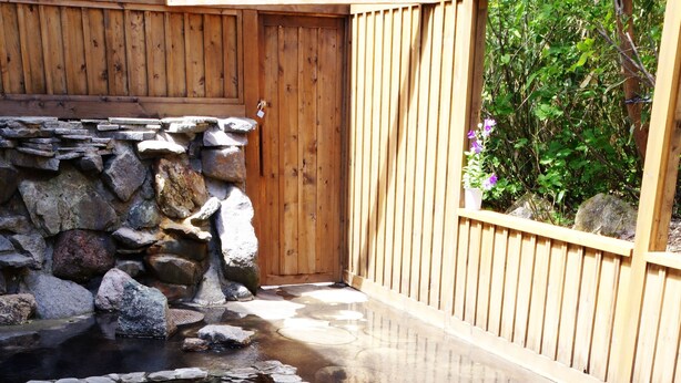 A stone-lined pool with a wooden fence and a wooden wall in the background. - K's House Hokkaido - Asahidake Onsen Hostel (Higashikawa)