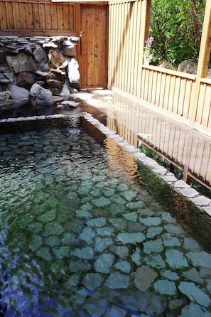 Une piscine bordée de pierres, avec une clôture en bois et un mur en bois en arrière-plan.