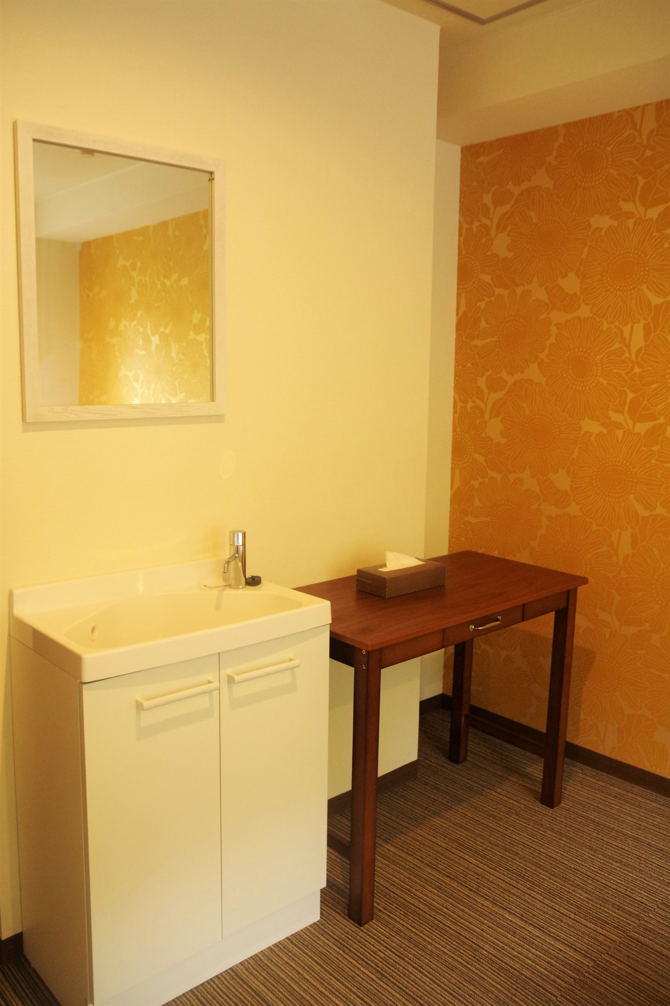 A small bathroom with a white sink, a mirror, and a wooden table with a tissue box.