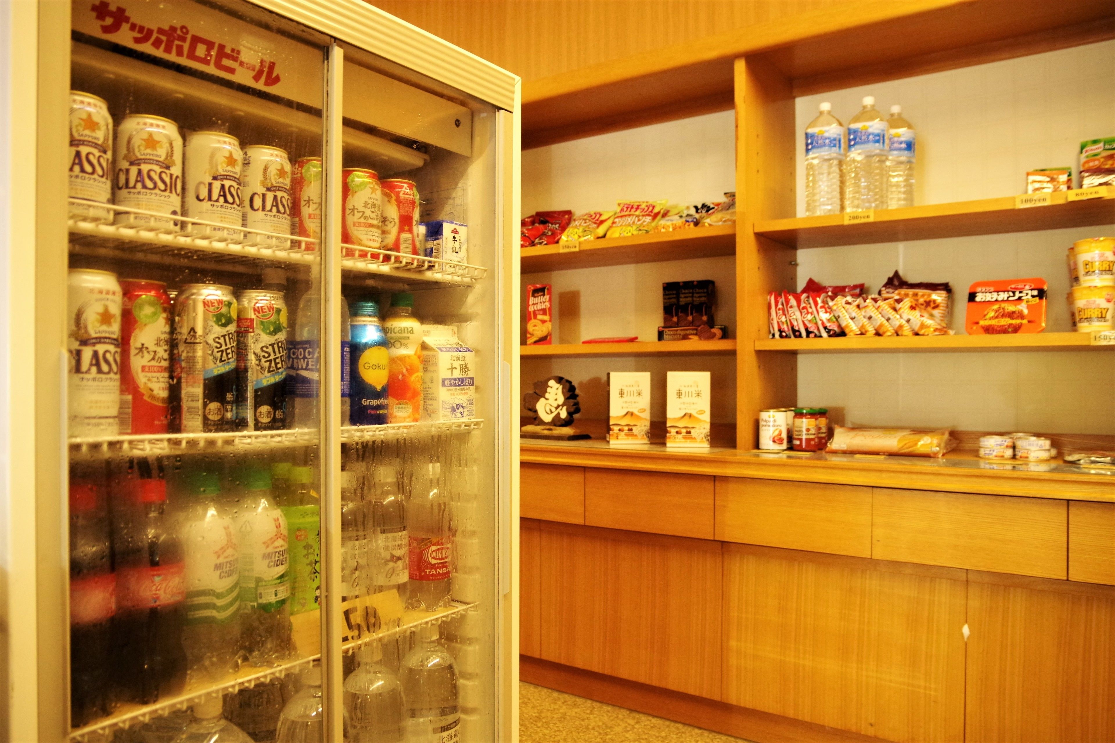 A vending machine stocked with various beverages and snacks, a wooden counter with packaged goods, and a shelf with bottled water.