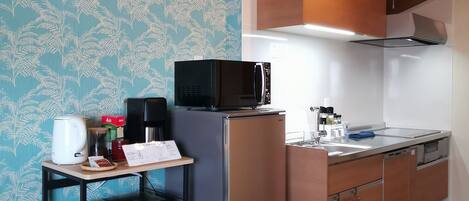 Una cocina compacta con microondas, refrigerador y una pequeña encimera. Se observa una repisa con utensilios de cocina y un revestimiento de pared estampado.