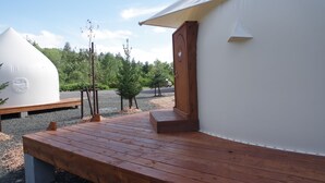 A wooden deck leading to a white tent with a door, surrounded by trees and a gravel path. - K's House Hokkaido - Asahidake Onsen Hostel (Higashikawa)