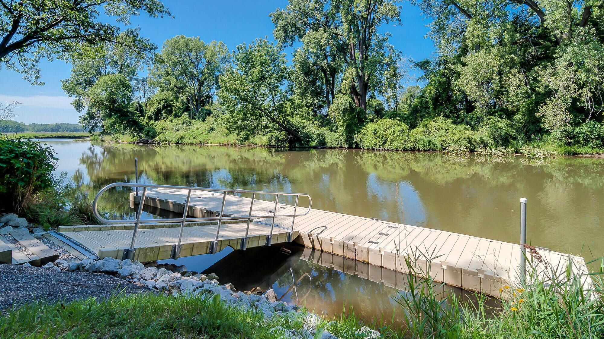 A wooden dock extending into a calm river, surrounded by lush greenery and trees.