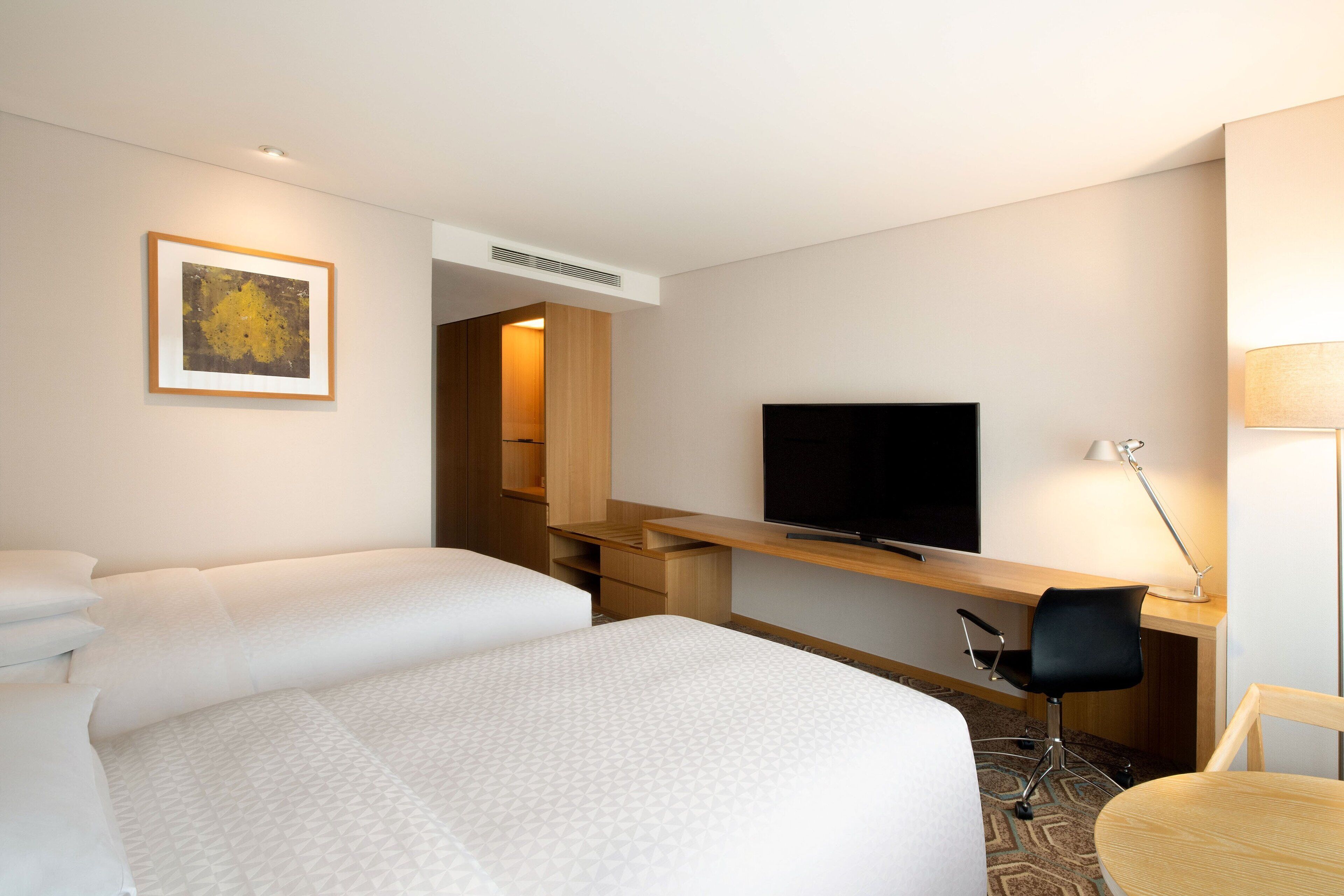 A hotel room with two beds, a TV, a desk, and a chair.