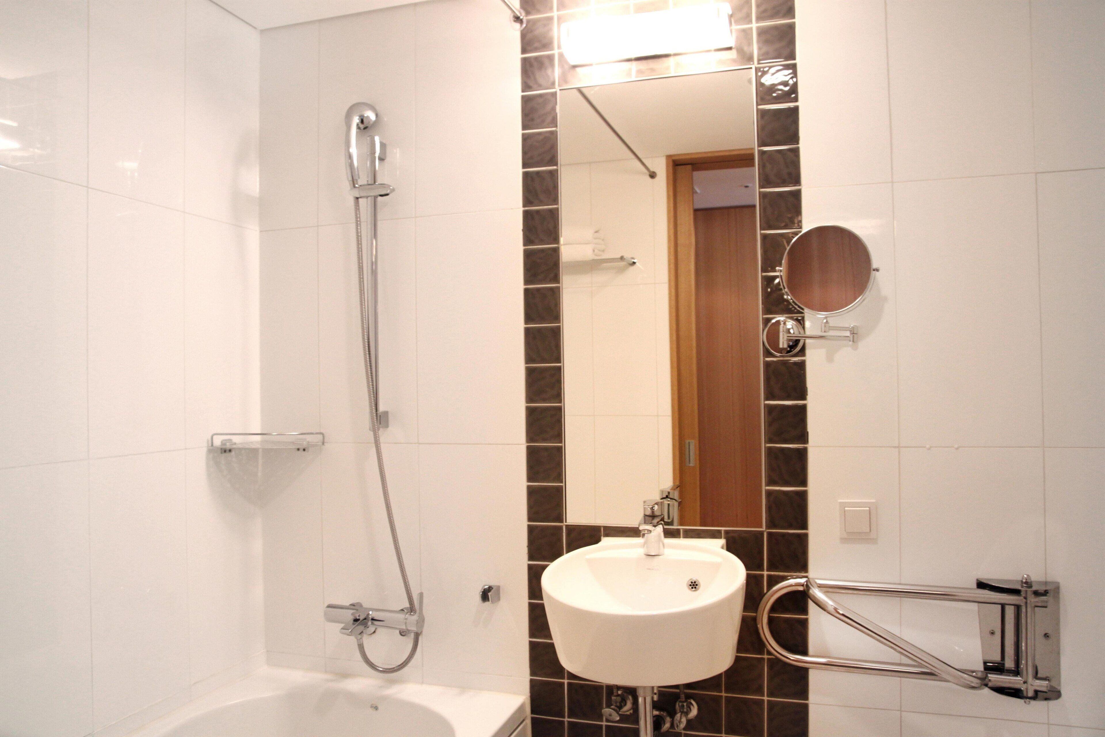 A bathroom with a white bathtub, a sink with a mirror, and a shower with a handheld showerhead.