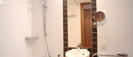 A bathroom with a white bathtub, a sink with a mirror, and a shower with a handheld showerhead.