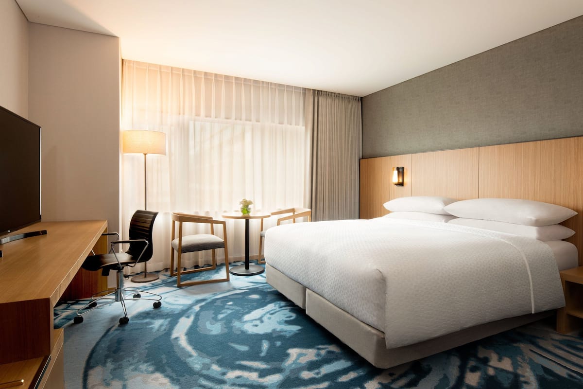 Ein Hotelzimmer mit einem großen Bett, einem Schreibtisch mit Stuhl, einem kleinen Tisch mit Lampe und einem Fernseher.