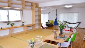A room with tatami flooring, a wooden table with chairs, a hammock, and a large window. - Clara Terrace (Ishigaki)
