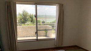 A room with three beds, a view of greenery and a building outside, and a lamp on the floor. - Clara Terrace (Ishigaki)