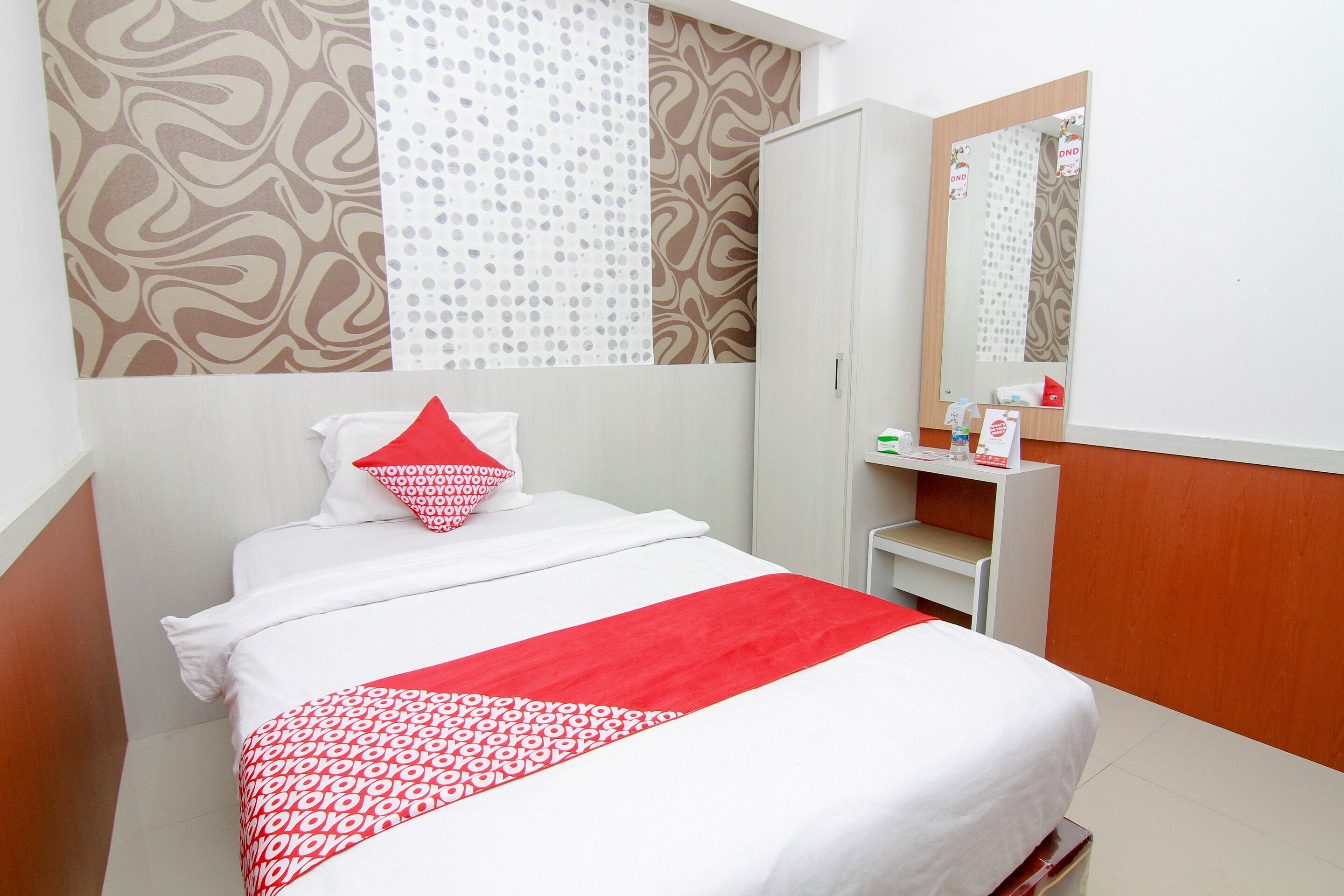 A hotel room with a bed, a wardrobe, a mirror, and a small table with toiletries.