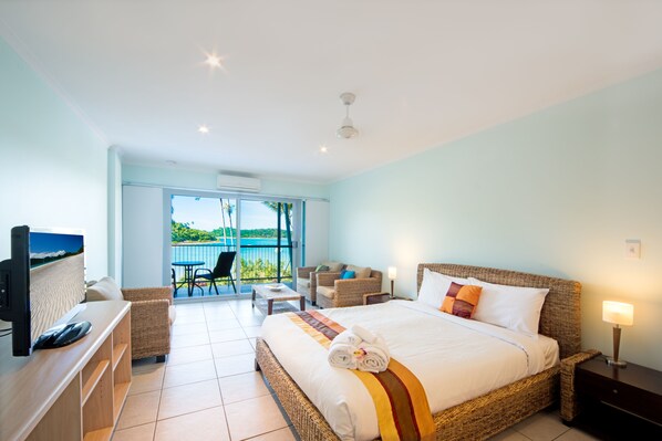 A hotel room with a large bed, a TV, a balcony with a view, and a dining area. - Baybliss Studio 1 (Shute Harbour)