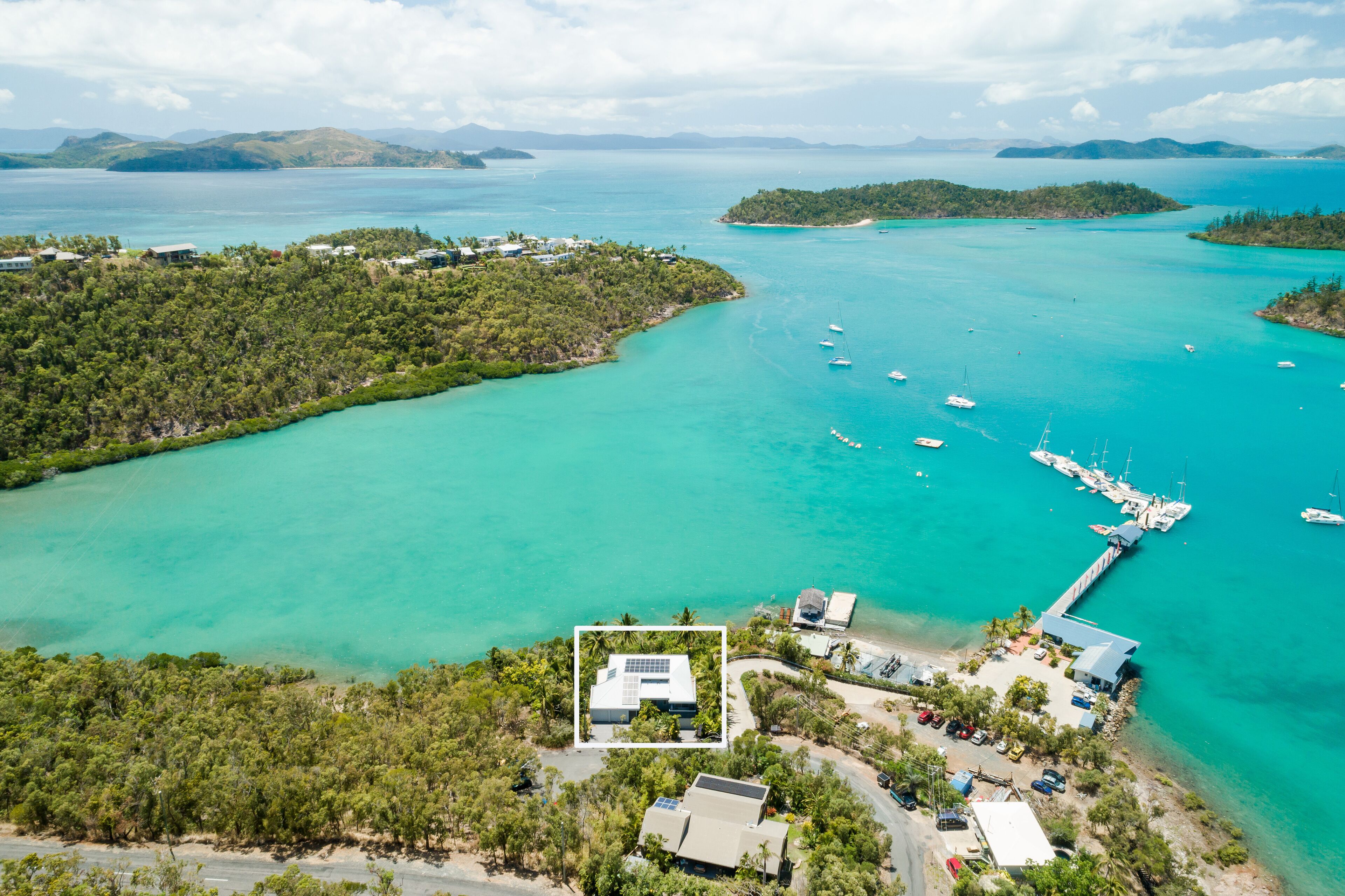 Vue aérienne d’une zone côtière avec un port de plaisance, des bateaux et un bâtiment équipé de panneaux solaires.