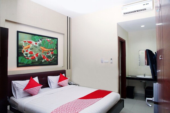 A hotel room with a bed, a painting of koi fish, a bathroom, and a refrigerator.