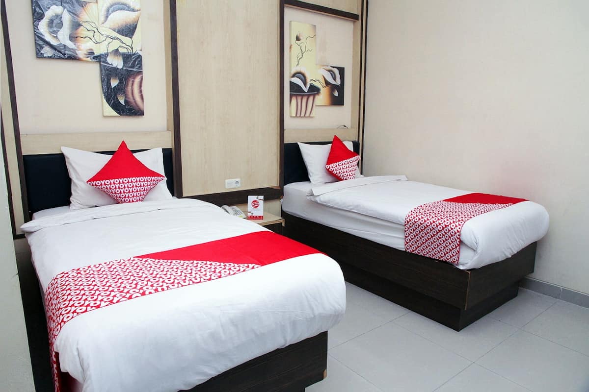 Two single beds with white bedding and red accents, a wooden headboard, and a wall-mounted telephone.