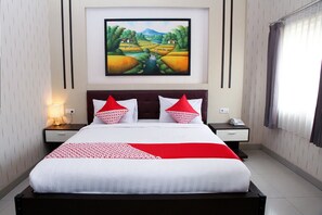 A neatly made bed with a red and white bedspread, two bedside tables with lamps, a painting of a landscape on the wall, and a window with curtains.
