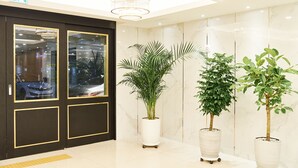 A modern lobby with a marble wall, a black door with glass panels, and potted plants. - Seattle B Hotel (Busan)