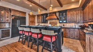 A kitchen with wooden cabinets, a black refrigerator, and a bar area with red cushioned chairs. - Luxury Townhome, Gourmet Kitchen, Hot Tub, Recreation, Great Location! (Deer Valley)