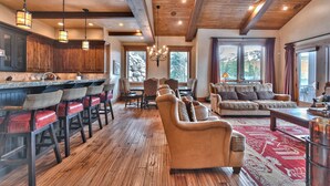 A spacious living area with a wooden floor, a large sofa, a dining table with chairs, and a kitchen area with wooden cabinets and bar stools. - Luxury Townhome, Gourmet Kitchen, Hot Tub, Recreation, Great Location! (Deer Valley)