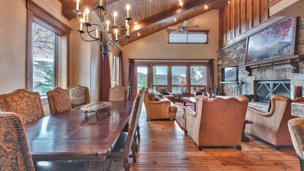 A spacious room with a large wooden dining table, comfortable seating, a stone fireplace, and large windows offering views of the outdoors. - Luxury Townhome, Gourmet Kitchen, Hot Tub, Recreation, Great Location! (Deer Valley)
