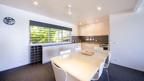 Una cocina moderna con armarios blancos, un ventanal con vistas a zonas verdes, una mesa de comedor con sillas y un reloj en la pared.