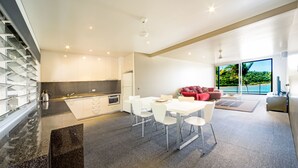 Una cocina moderna con armarios blancos, una zona de comedor con sillas blancas y un sofá rojo.