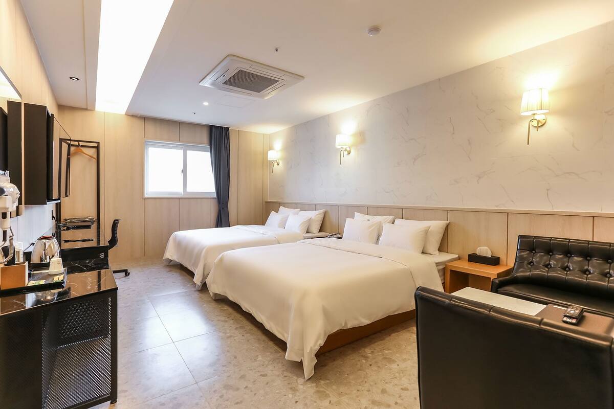A hotel room with two beds, a desk, a chair, and a sofa.