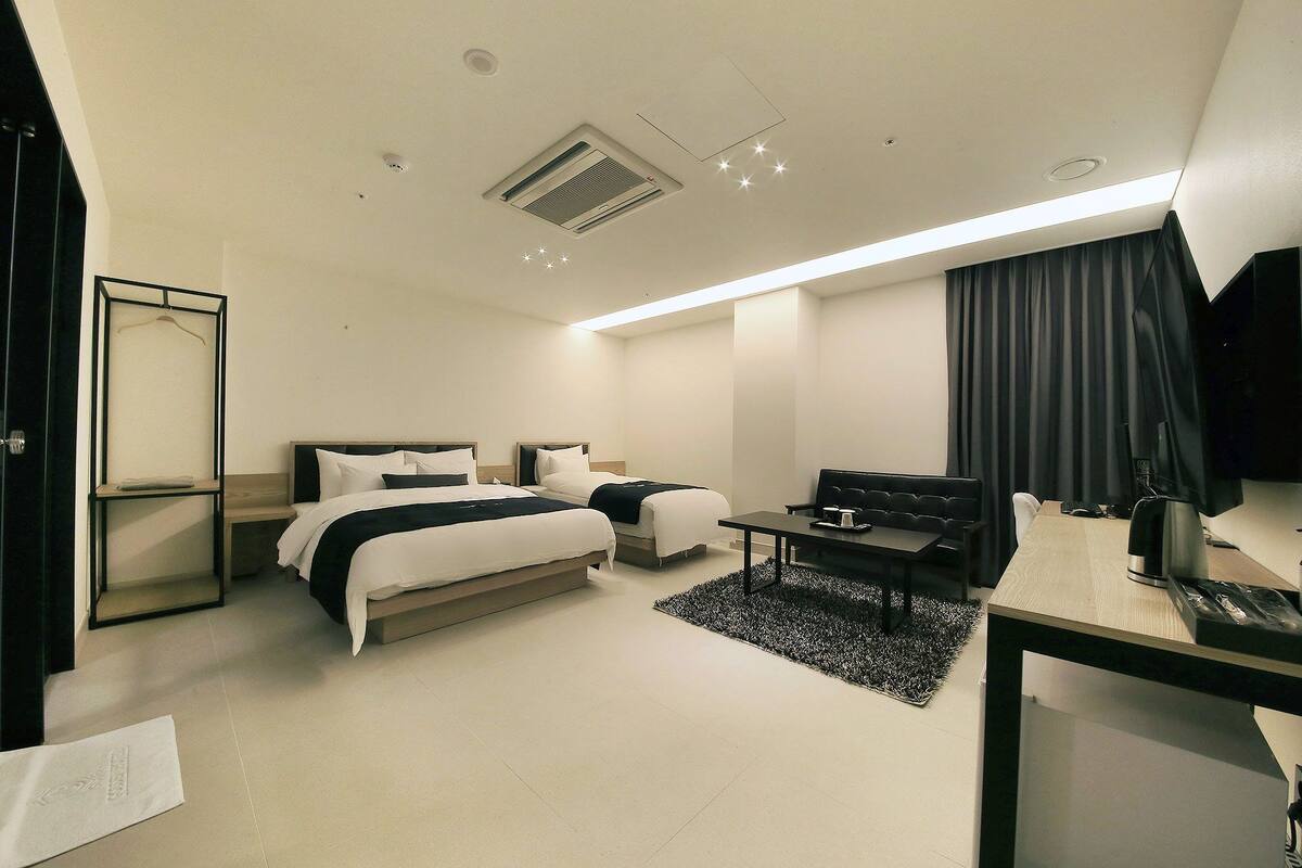 A modern hotel room with two beds, a desk, a chair, a TV, and a large window with curtains.
