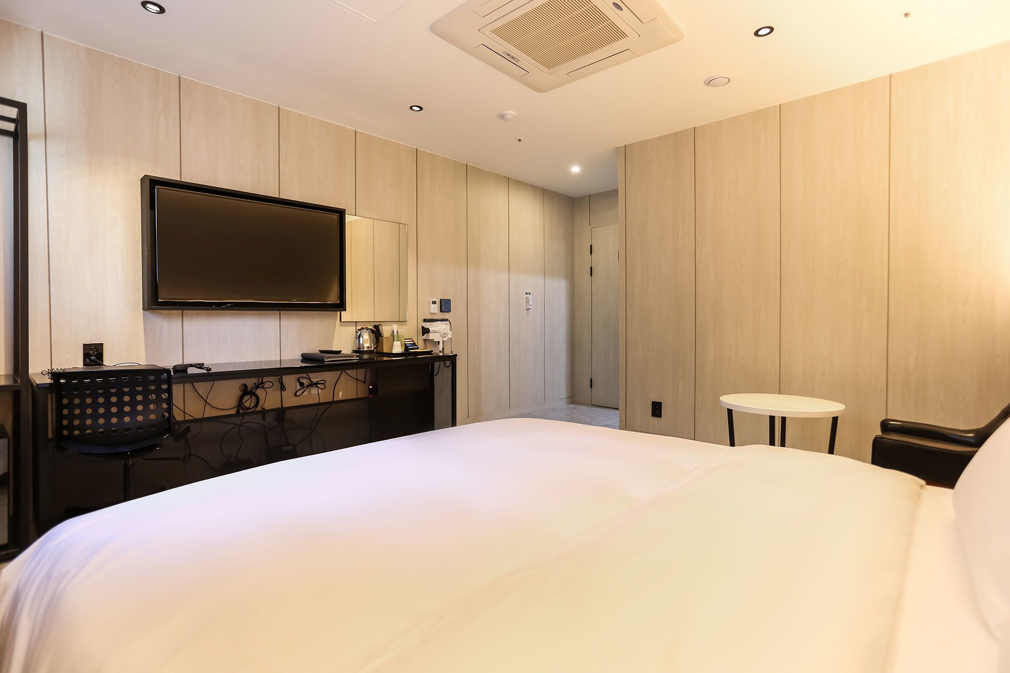 Et moderne hotelværelse med en stor seng, et skrivebord med et fladskærms-tv, et lille rundt bord og et spejl.