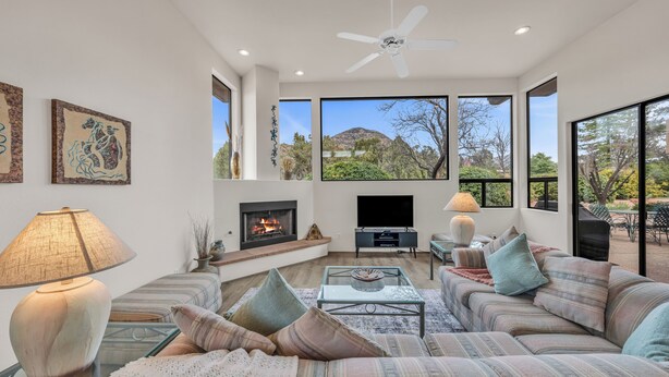 A modern living room with a fireplace, large windows, and a view of a mountain. - Santa Susana | West Sedona Townhome w/ Pool, Hot Tub & Red Rock Views (Sedona)