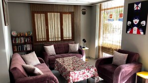 A living room with two purple sofas, a floral table, and a bookshelf. - Meltem Hotel (Konyaalti)